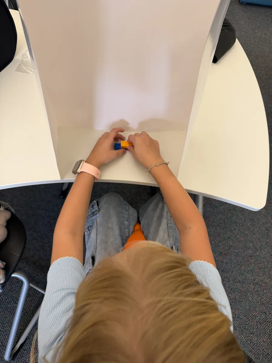 A student's hands snapping blocks together behind the wall, seen from above